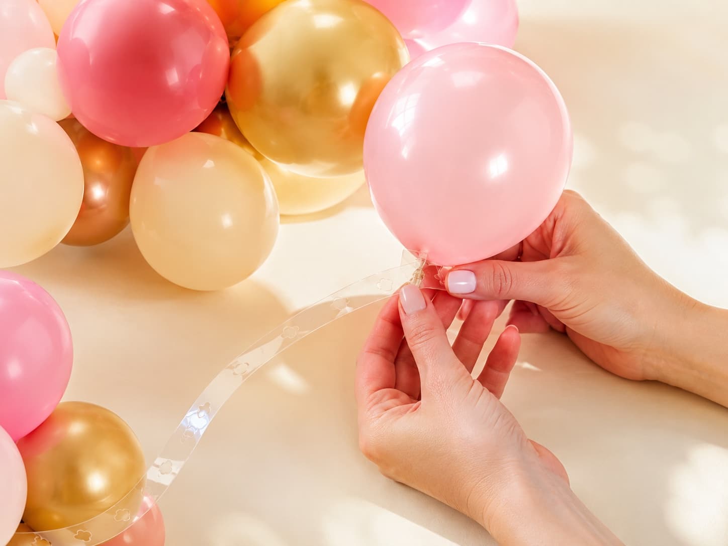 Hands attaching air-filled balloons onto a balloon tape strip to build a garland — no helium needed
